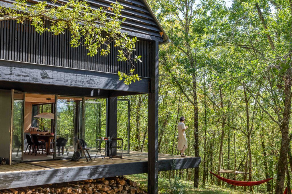 une maison en bois noire dans les arbres avecune terrasse en porte- a faux